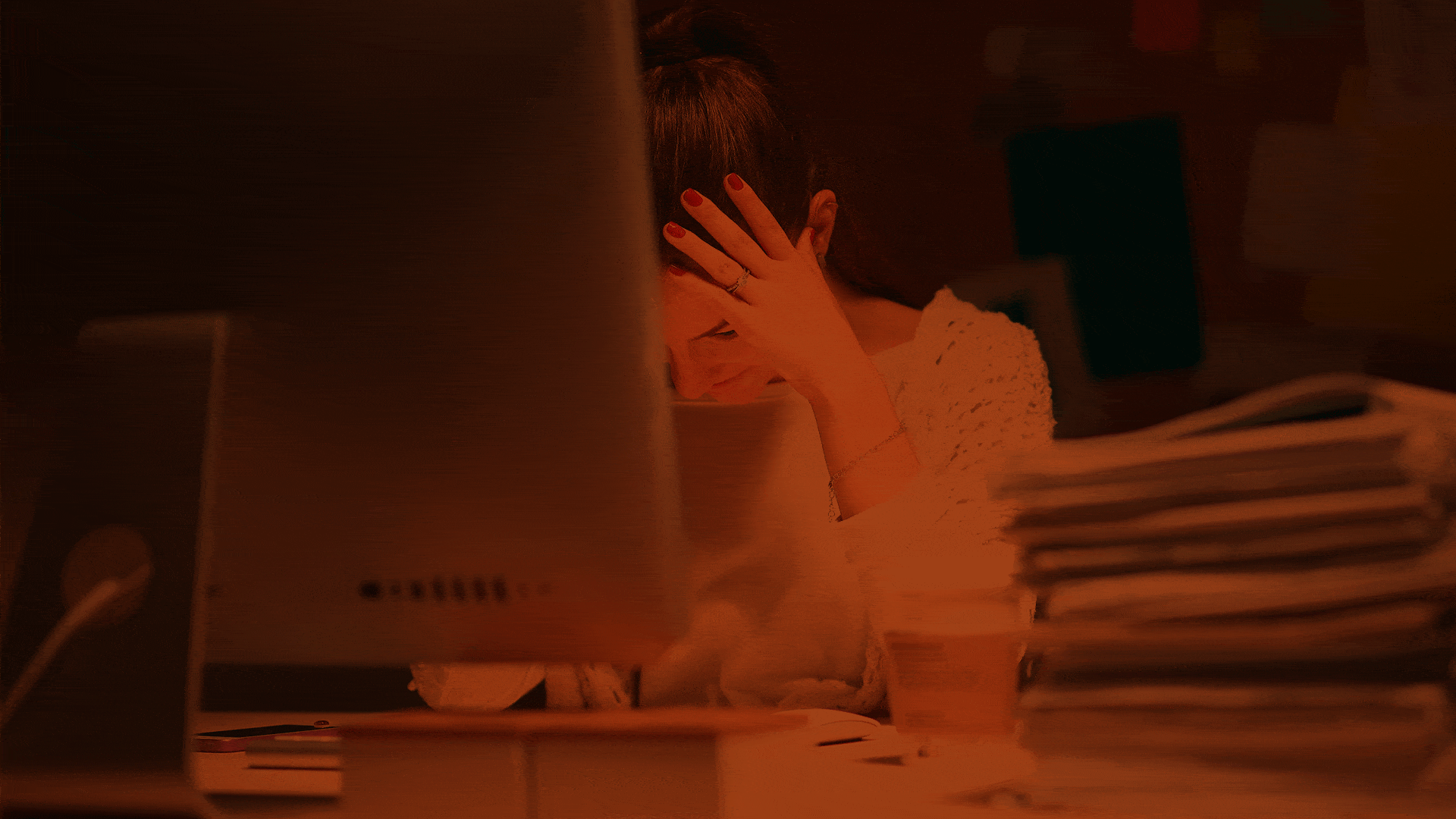 Eine gestresste Frau sitzt am Computer und hält sich die Hand vor dem Gesicht.